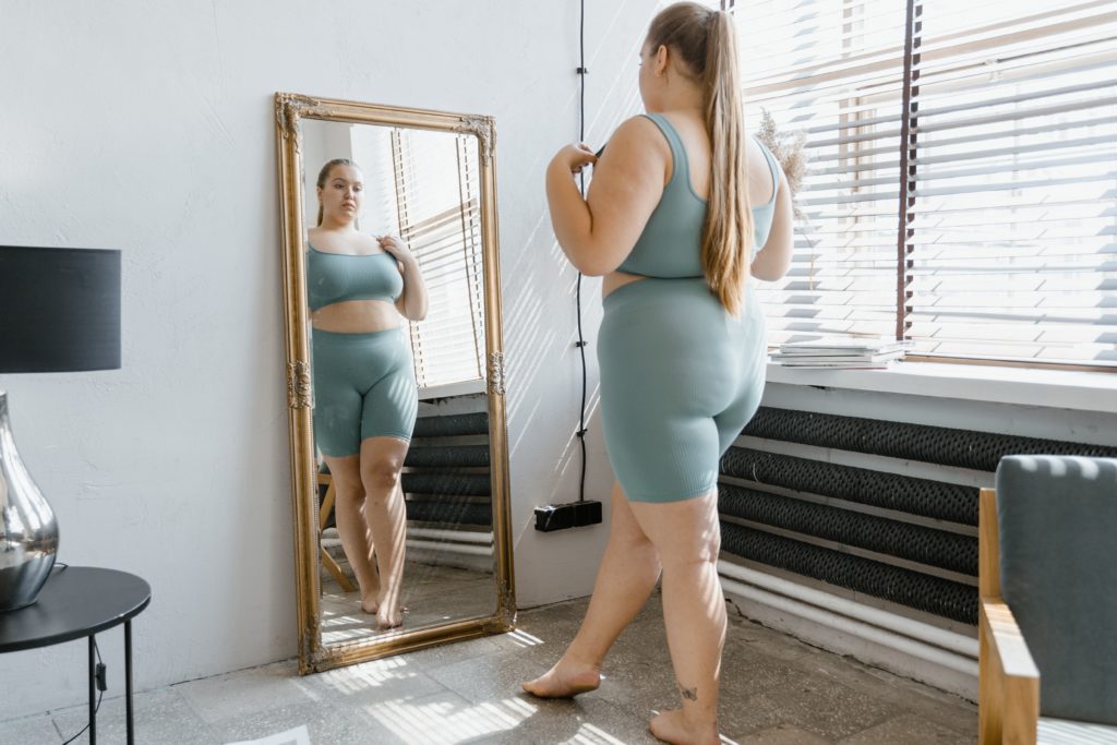 Woman looking in a mirror assessing her body through low self-esteem