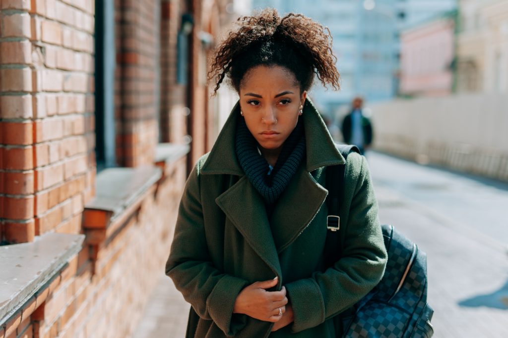 Woman in Green Coat Standing on Sidewalk suffering with low self-esteem