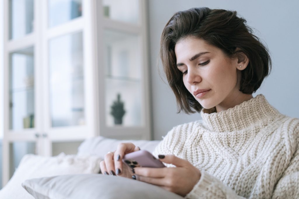 A Woman in White Knitted Sweater Looking at social media with a single tear running down her face as it effects her self-esteem
