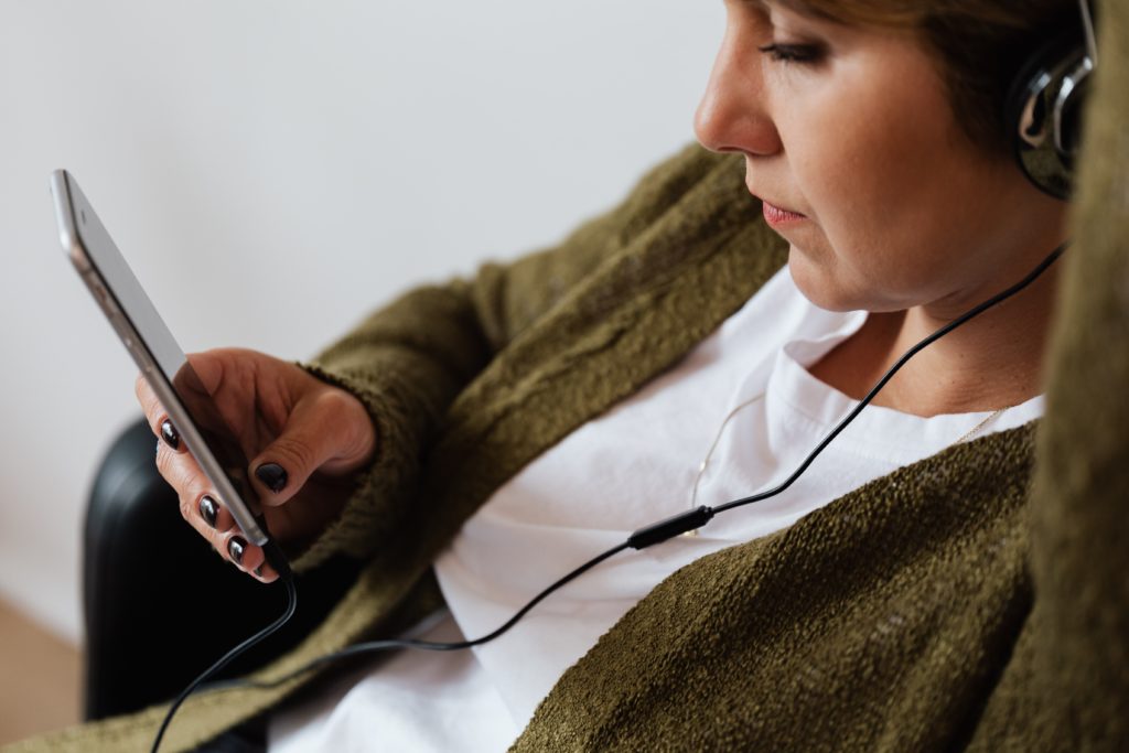 Woman wearing a green cardigan and white t-shirt, with headphones in scrolling social media on her phone.