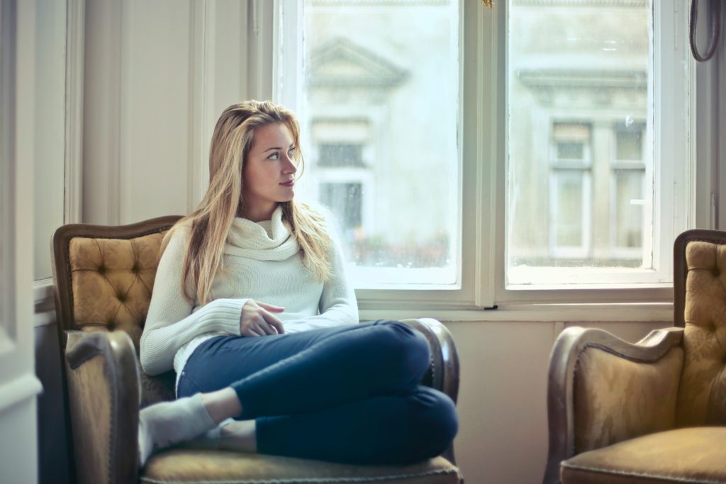 Woman wearing white jumper and jeans, sat down taking time to think about her social comparison