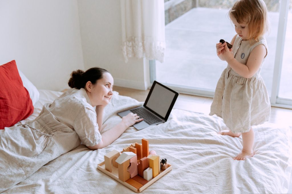 Woman lying on a bed, watching her daughter play admiring the life she has turning her social comparison into a positive one.