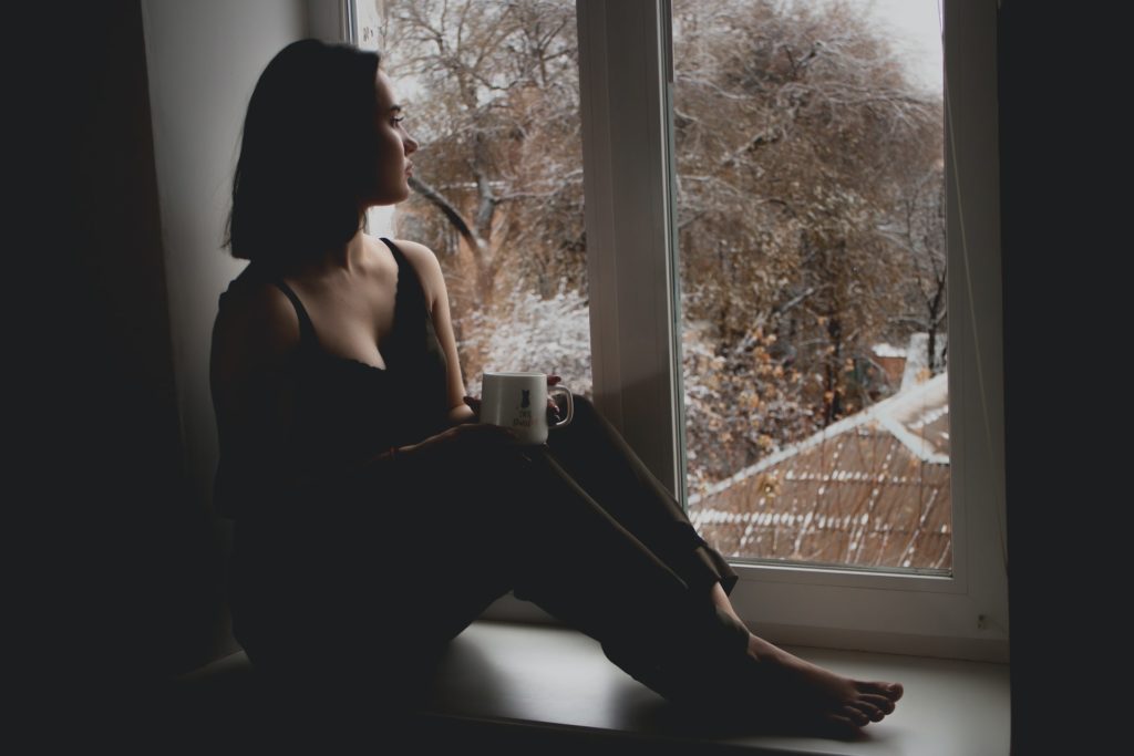 Woman sat in the window feeling weak due to having no self compassion for herself