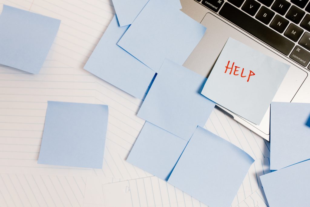 Many blue post-it notes scattered on a desk with a singular post-it note having the words HELP in red.