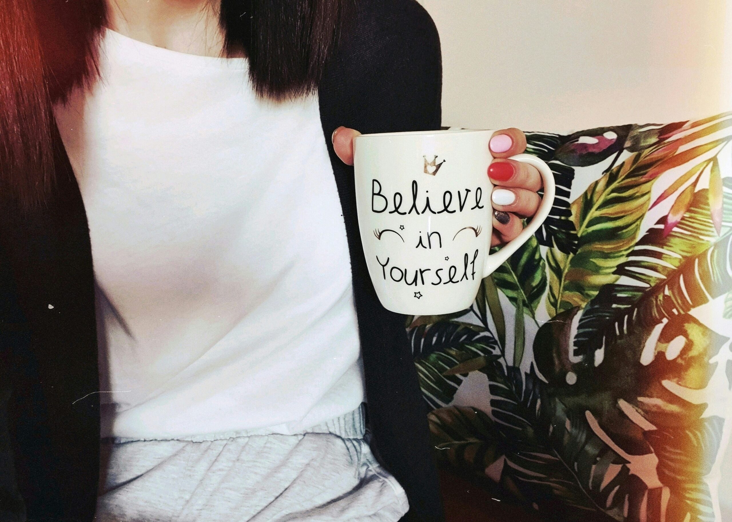 woman wearing black cardigan holding mug that says 'believe in yourself'