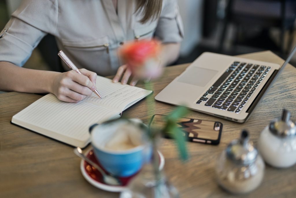 person writing on a notebook beside macbook to improve self-esteem and bodyh image