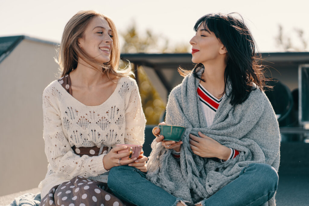 Two women talking to one another holding cups of tea discussing practising self-care