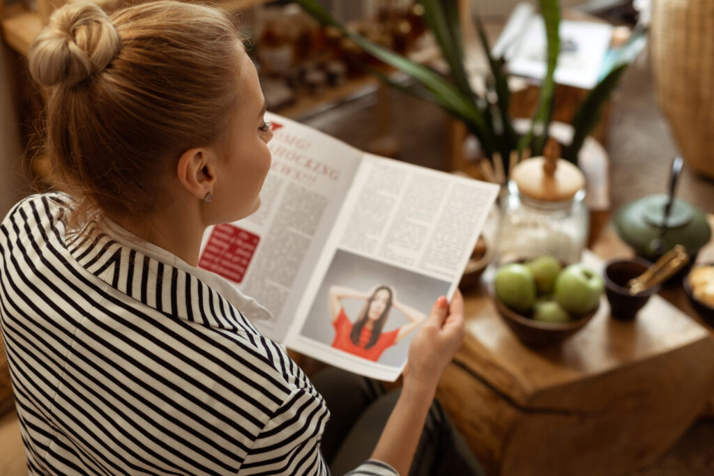 A woman holding a magazine looking at the unrealistic expectations of beauty put on women by societal standards and this has an impact on her body image and self-esteem.
