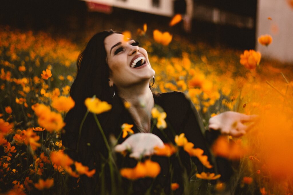 Happy smiling woman connecting with nature in the great outdoors. Pictures shows her surrounded by vibrant orange flowers.  