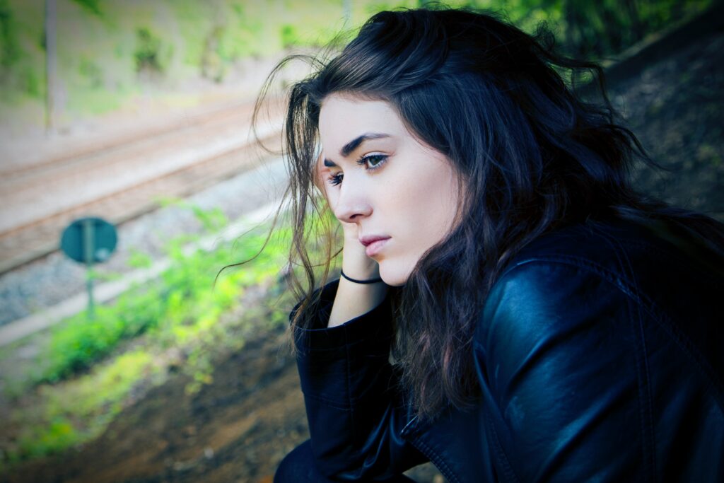 Woman outdoors in black jacket looking sad and thoughtful as she listens to her negative thoughts 