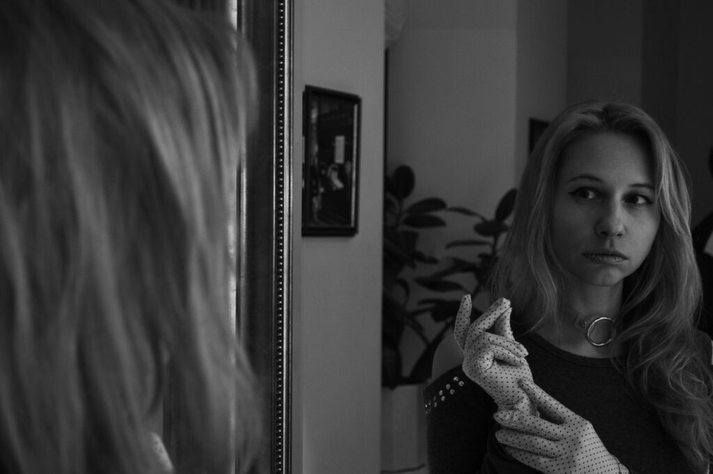 woman looking pensively at her reflection in the mirror and possibly battling negative thoughts as she checks her appearance