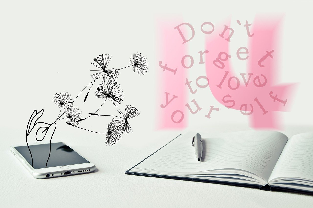phone and notebook with pen, with words floating above that say 'don't forget to love yourself'