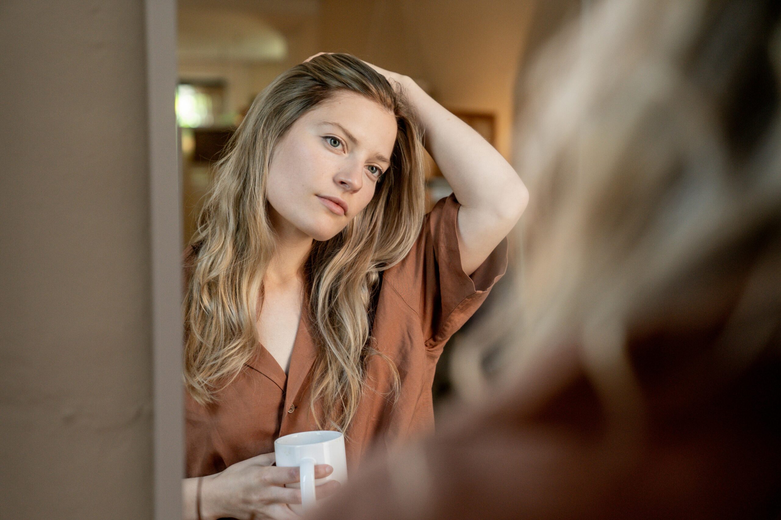 Woman looking at reflection in mirror with self-doubt