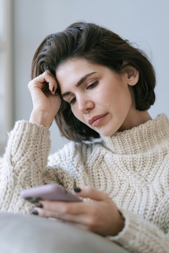 woman looking at smartphone unhappily, symbolising reducing distractions and focusing on self-worth.